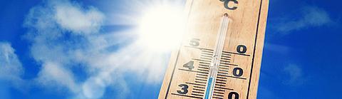 Ein Thermometer vor einem blauen Himmel mit Sonne zeigt über 30 Grad Celsius an.