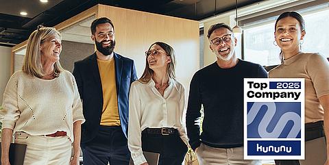 Kollegen stehen im Büro zusammen und lachen.