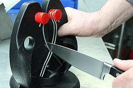 Koch schleift Messer mit einem Messerschleifgerät